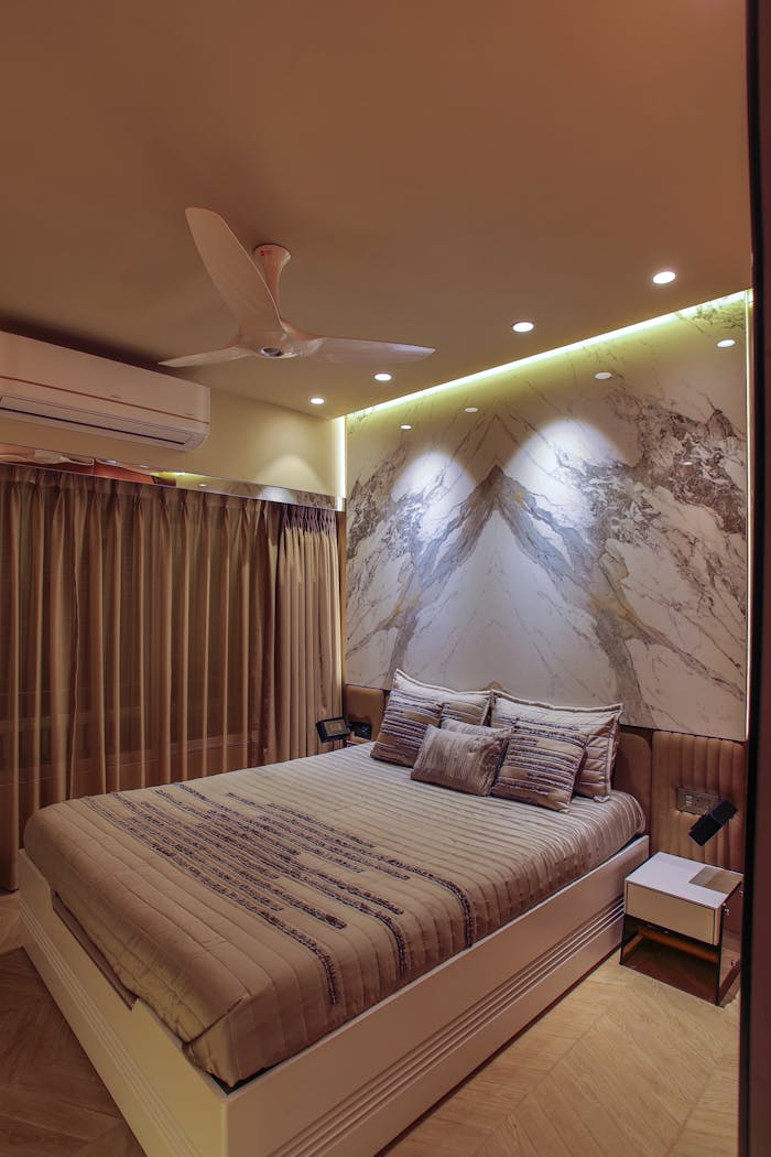 Stylish bedroom with ambient lighting and contemporary decor features a ceiling fan and artistic wall design.